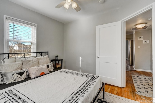 bedroom with freestanding refrigerator, visible vents, ceiling fan, and wood finished floors