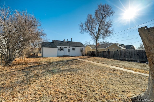 rear view of house with stucco siding, fence, and a lawn