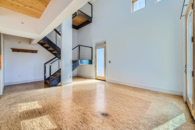 unfurnished living room with speckled floor, a high ceiling, wood ceiling, baseboards, and stairs