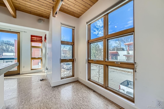 doorway to outside with baseboards, wooden ceiling, beamed ceiling, speckled floor, and a wealth of natural light