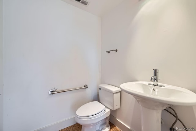 half bathroom with toilet, a sink, visible vents, and baseboards