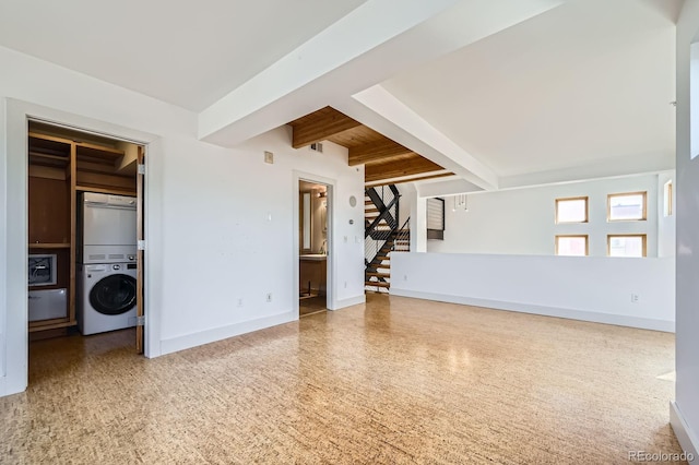 unfurnished living room with speckled floor, baseboards, stairs, beam ceiling, and stacked washer and clothes dryer