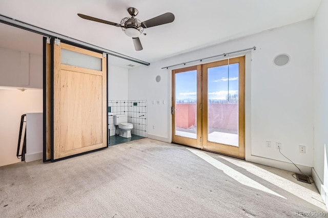 unfurnished bedroom with access to exterior, carpet flooring, ceiling fan, and a barn door