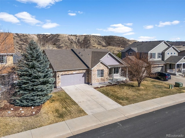 traditional home featuring a front lawn, stone siding, a mountain view, concrete driveway, and an attached garage