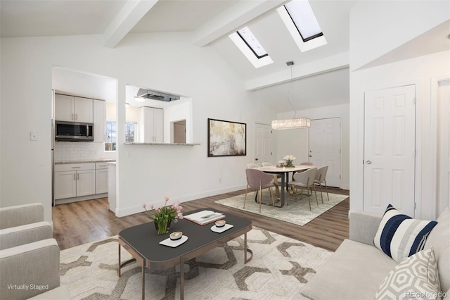 living room featuring light hardwood / wood-style floors, a skylight, a chandelier, high vaulted ceiling, and beam ceiling