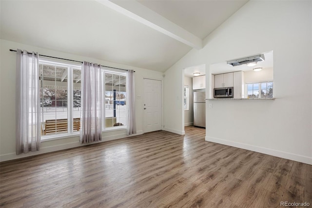 unfurnished living room with light hardwood / wood-style flooring and vaulted ceiling with beams