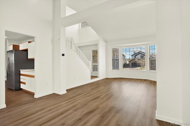 unfurnished living room featuring wood finished floors, baseboards, stairs, and high vaulted ceiling