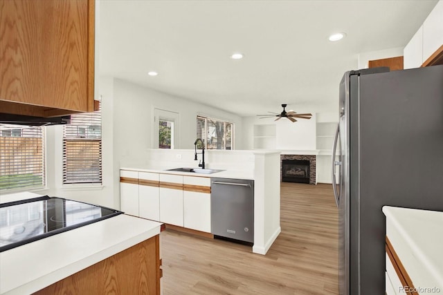 kitchen with a peninsula, light wood finished floors, a sink, stainless steel appliances, and ceiling fan