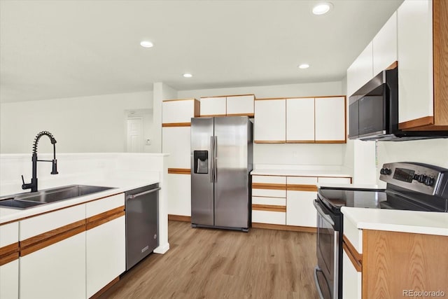 kitchen with light wood-style flooring, stainless steel appliances, a sink, white cabinetry, and light countertops