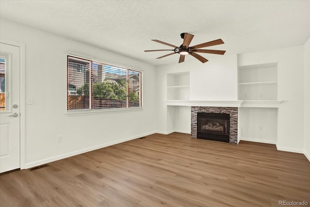 unfurnished living room with wood finished floors, a ceiling fan, visible vents, baseboards, and a stone fireplace