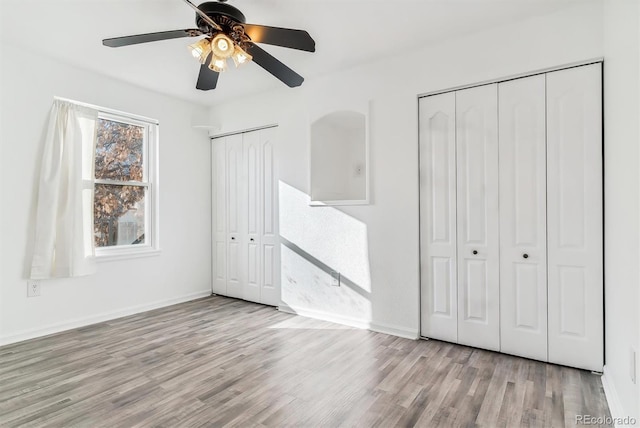 unfurnished bedroom with ceiling fan, light hardwood / wood-style flooring, and two closets