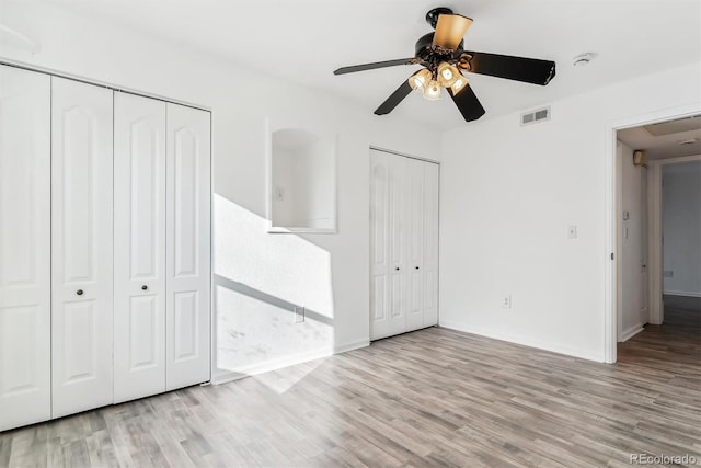 unfurnished bedroom featuring light hardwood / wood-style flooring, ceiling fan, and multiple closets