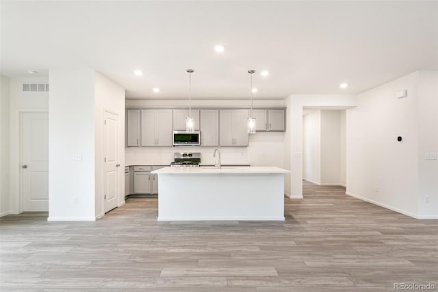 kitchen with a kitchen island with sink, sink, decorative light fixtures, gray cabinets, and appliances with stainless steel finishes