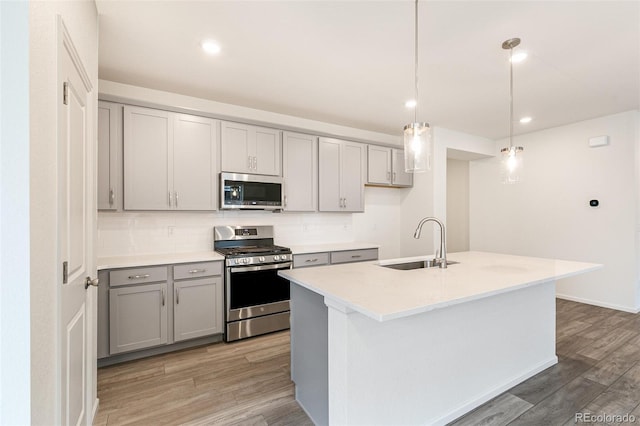 kitchen with a center island with sink, light hardwood / wood-style flooring, stainless steel appliances, sink, and decorative light fixtures