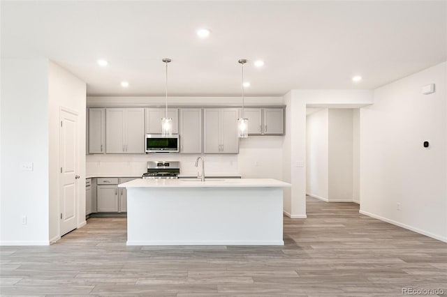 kitchen featuring hanging light fixtures, a center island with sink, appliances with stainless steel finishes, gray cabinets, and light hardwood / wood-style floors