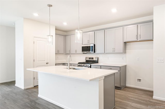 kitchen featuring appliances with stainless steel finishes, sink, hardwood / wood-style floors, decorative light fixtures, and a kitchen island with sink