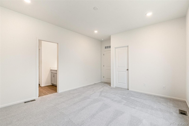 unfurnished bedroom featuring light colored carpet and ensuite bath