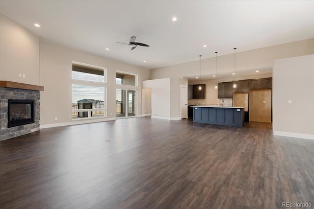 unfurnished living room with a stone fireplace, dark wood-type flooring, sink, and ceiling fan