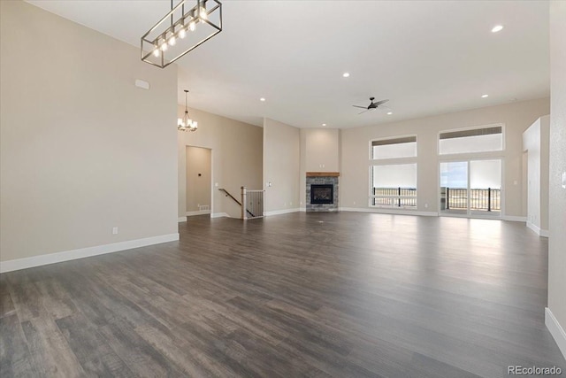 unfurnished living room featuring a stone fireplace, dark wood-type flooring, and ceiling fan with notable chandelier