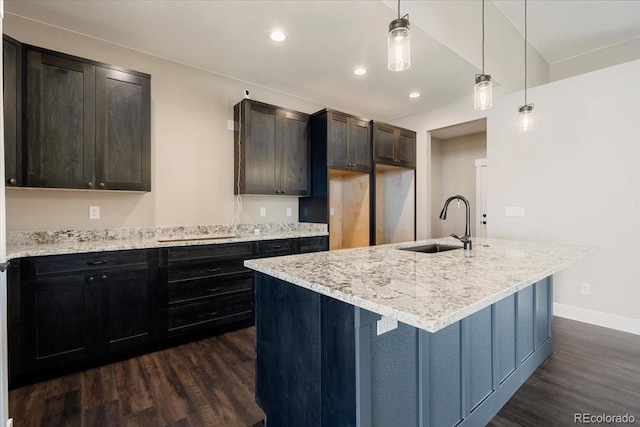 kitchen featuring dark hardwood / wood-style flooring, decorative light fixtures, light stone countertops, and an island with sink