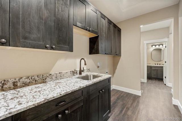 kitchen with light stone counters, dark brown cabinetry, dark hardwood / wood-style flooring, and sink