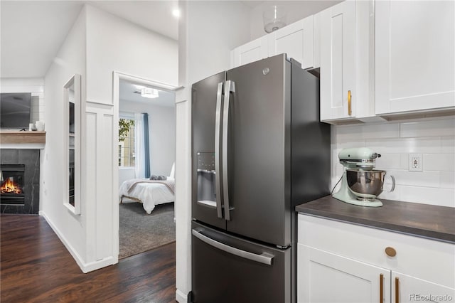 kitchen with white cabinetry, stainless steel refrigerator with ice dispenser, a tiled fireplace, tasteful backsplash, and dark hardwood / wood-style flooring