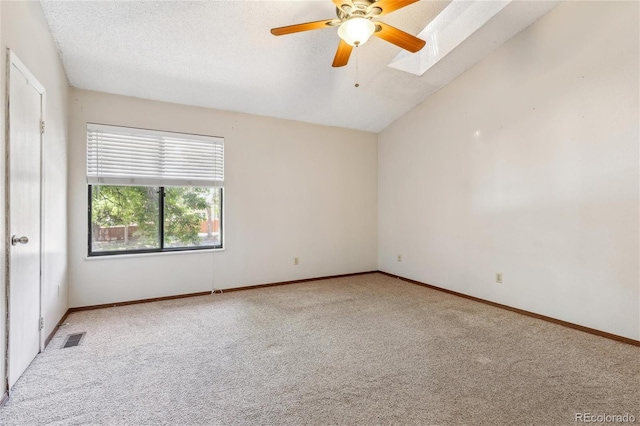 carpeted empty room featuring lofted ceiling with skylight, a textured ceiling, and ceiling fan