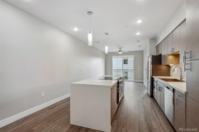 kitchen featuring a center island with sink, stainless steel appliances, tasteful backsplash, dark wood-type flooring, and a sink