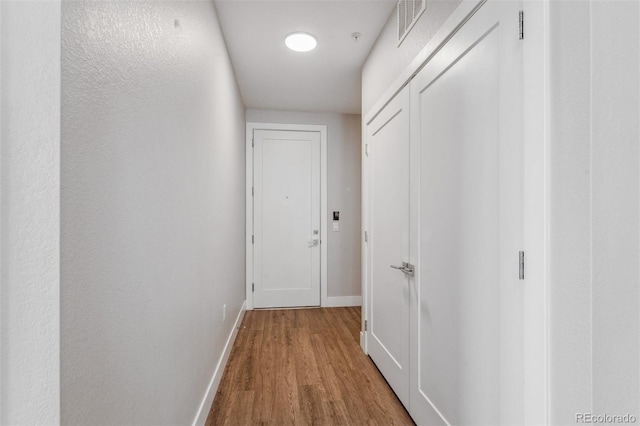 hall with visible vents, baseboards, and wood finished floors