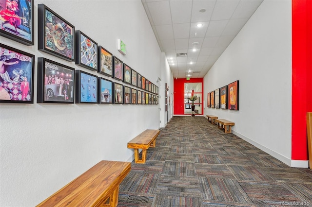 hall featuring a paneled ceiling, carpet flooring, and baseboards