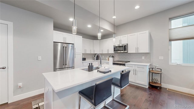 kitchen featuring appliances with stainless steel finishes, dark wood-type flooring, white cabinets, pendant lighting, and a kitchen bar