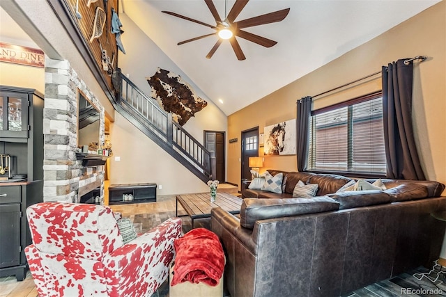 living area featuring lofted ceiling, ceiling fan, wood finished floors, stairs, and a stone fireplace