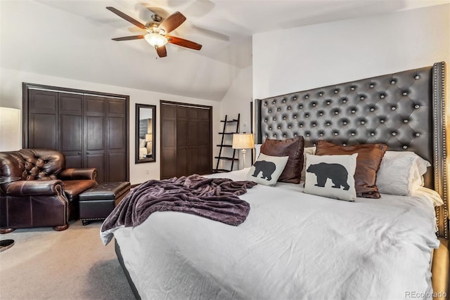 bedroom featuring ceiling fan, light colored carpet, vaulted ceiling, and two closets