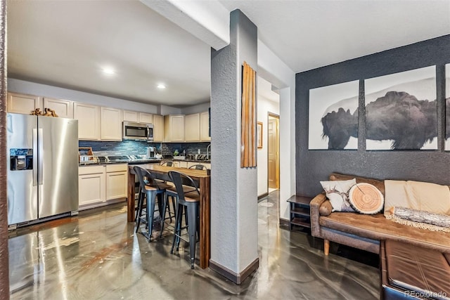 kitchen with a textured wall, stainless steel appliances, dark countertops, and backsplash