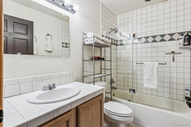 full bathroom featuring toilet, shower / bath combination with glass door, vanity, and a textured wall