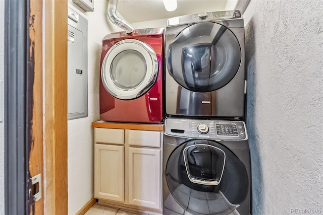 clothes washing area with a textured wall, cabinet space, and stacked washer / drying machine