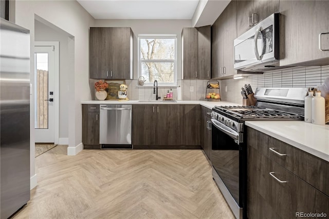 kitchen with sink, appliances with stainless steel finishes, tasteful backsplash, dark brown cabinetry, and light parquet flooring