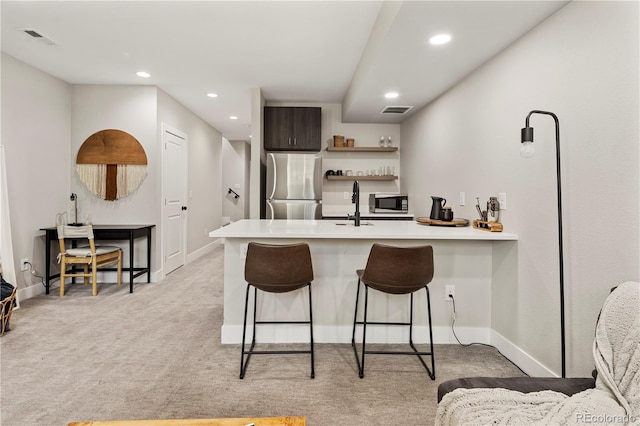 kitchen featuring a kitchen breakfast bar, stainless steel appliances, dark brown cabinetry, light colored carpet, and kitchen peninsula