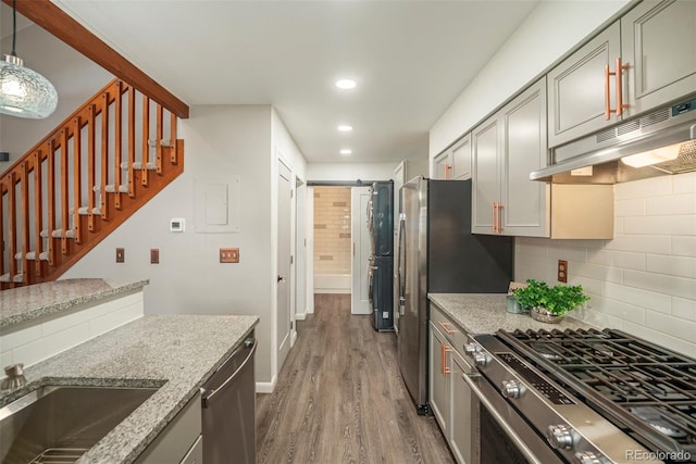 kitchen featuring tasteful backsplash, dark wood-style flooring, appliances with stainless steel finishes, under cabinet range hood, and light stone counters