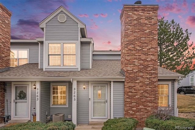 townhome / multi-family property featuring central AC unit, roof with shingles, and a chimney