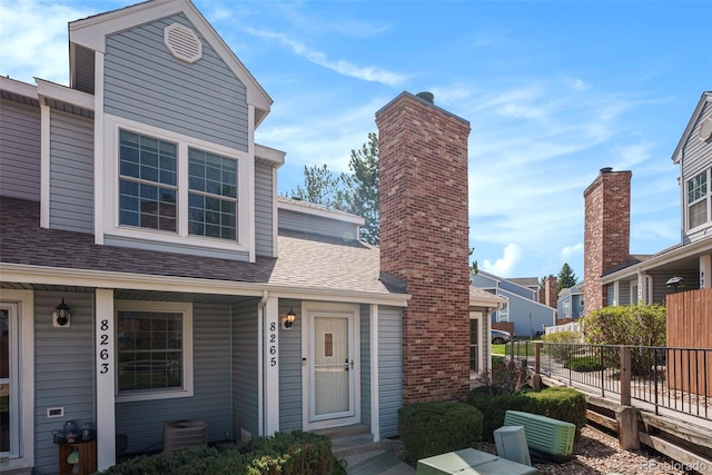 view of front of house featuring central air condition unit, a chimney, a shingled roof, and fence