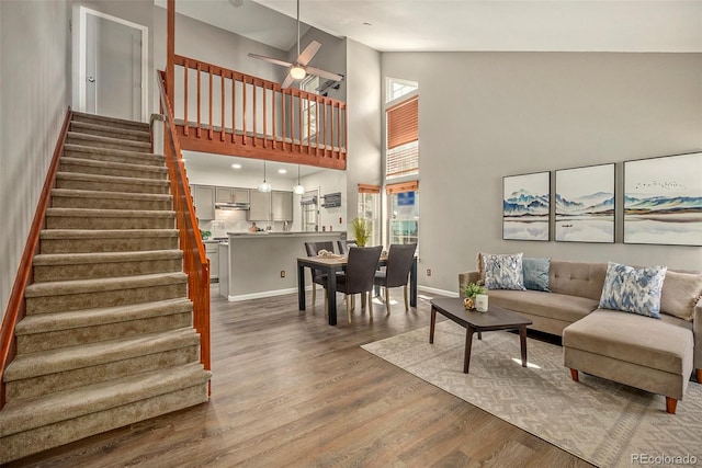 living area featuring ceiling fan, stairway, a high ceiling, and wood finished floors