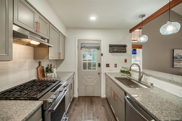 kitchen with under cabinet range hood, appliances with stainless steel finishes, a sink, gray cabinetry, and dark wood-style floors