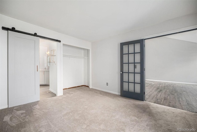 unfurnished bedroom featuring ensuite bathroom, baseboards, carpet, and a barn door