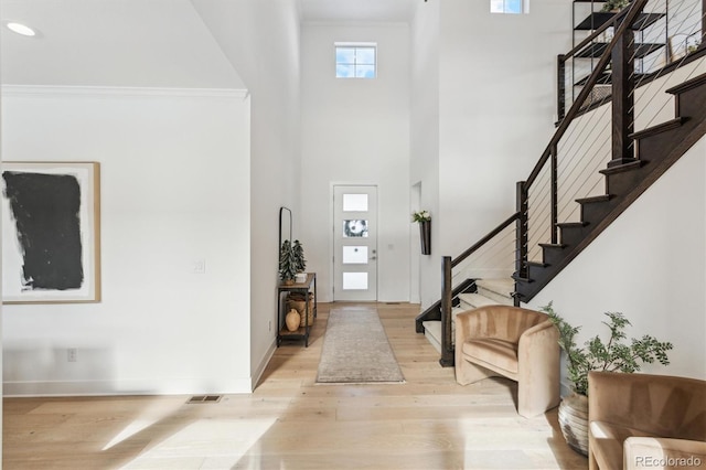 entrance foyer featuring a high ceiling, crown molding, and light wood-type flooring