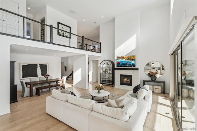 living room with a tiled fireplace, a towering ceiling, and light wood-type flooring