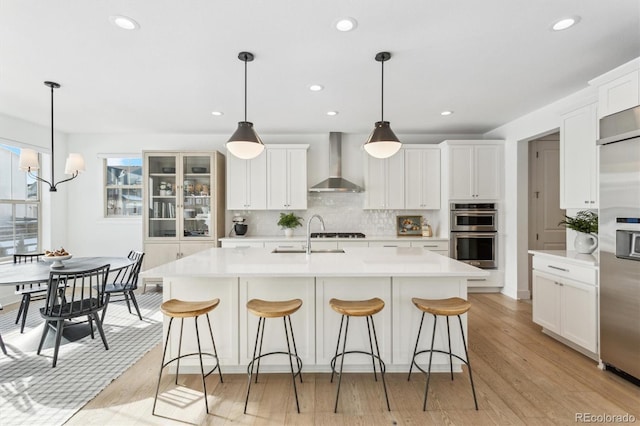 kitchen featuring sink, appliances with stainless steel finishes, white cabinetry, decorative light fixtures, and wall chimney exhaust hood