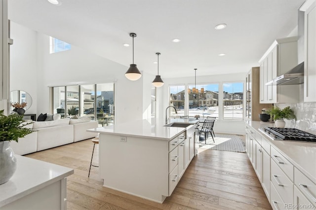 kitchen with white cabinetry, wall chimney range hood, decorative light fixtures, and a center island with sink