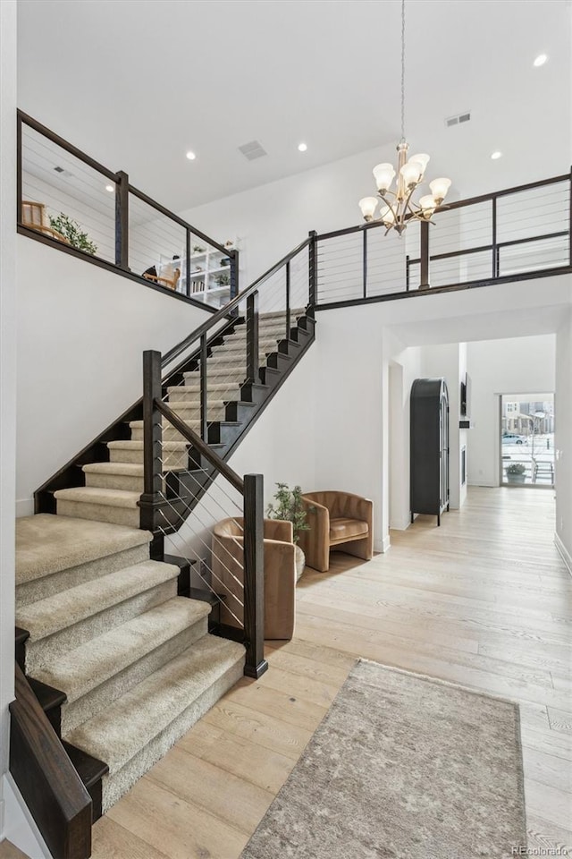 stairway with hardwood / wood-style floors, a notable chandelier, and a high ceiling