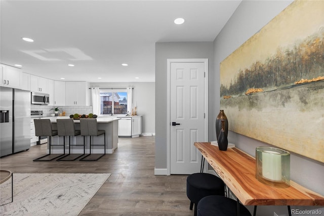 kitchen featuring tasteful backsplash, wood-type flooring, a kitchen breakfast bar, stainless steel appliances, and white cabinets